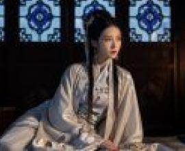 古代女性，一位身穿長裙、頭戴黑色長髮蝴蝶結的女子坐在床上。