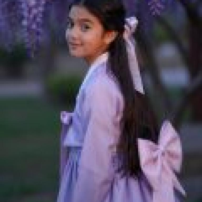 International students in South Korea，A girl with a purple dress and bow standing in front of a tree.