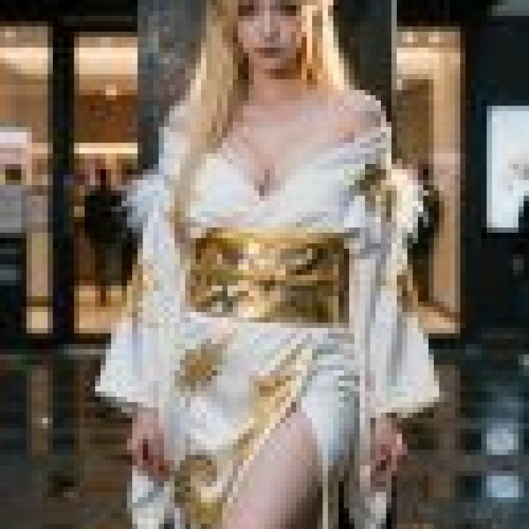 身穿白色和金色長袍的女子站在柱子旁。