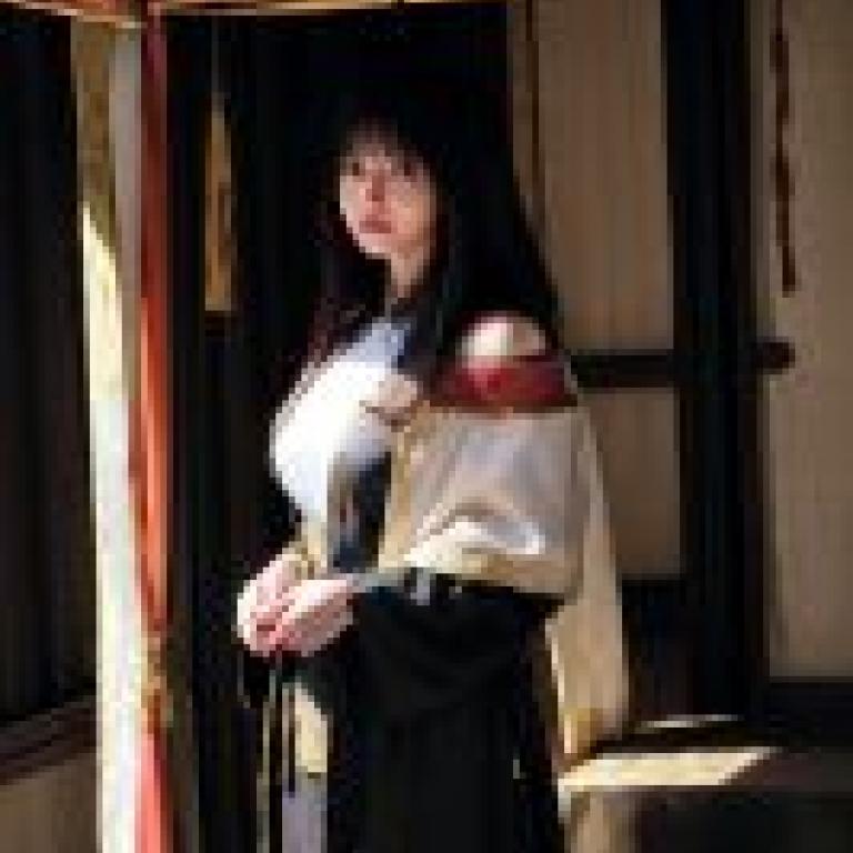 KyokofukadaA woman in a robe and scarf stands near red curtains.