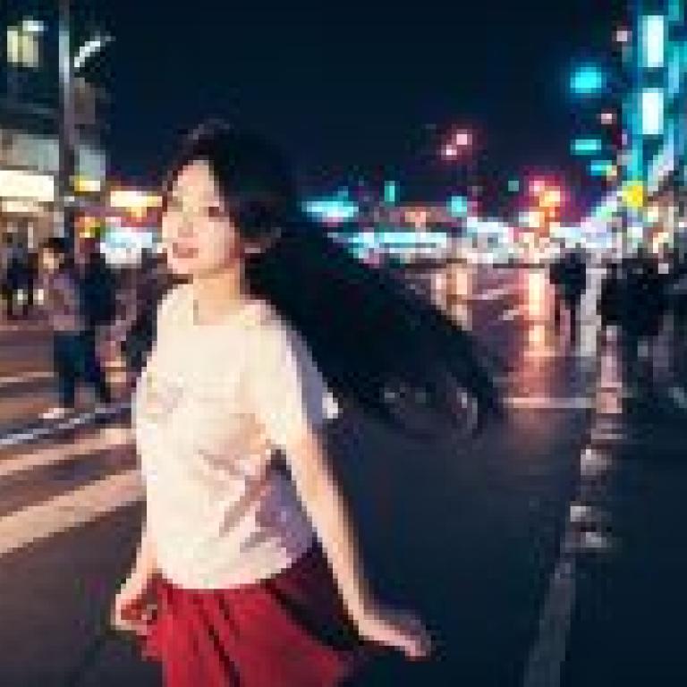 出雲風子 不死族 厄運 神經達文西 一位身穿白衣、腰間繫著紅裙的女子站在人行道邊緣。