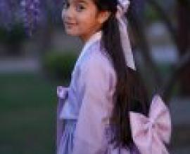 International students in South Korea，A girl with a purple dress and bow standing in front of a tree.