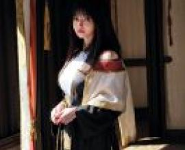 KyokofukadaA woman in a robe and scarf stands near red curtains.